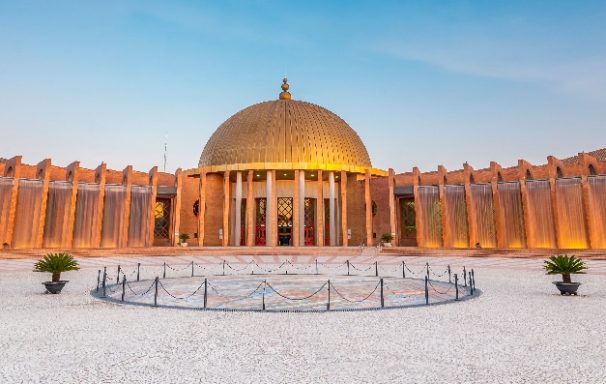 Edificio con cúpula dorada y columnas, rodeado de jardines al atardecer.