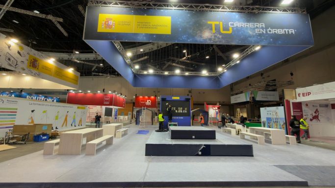 Stand de exhibición en construcción con trabajadores y áreas delimitadas.